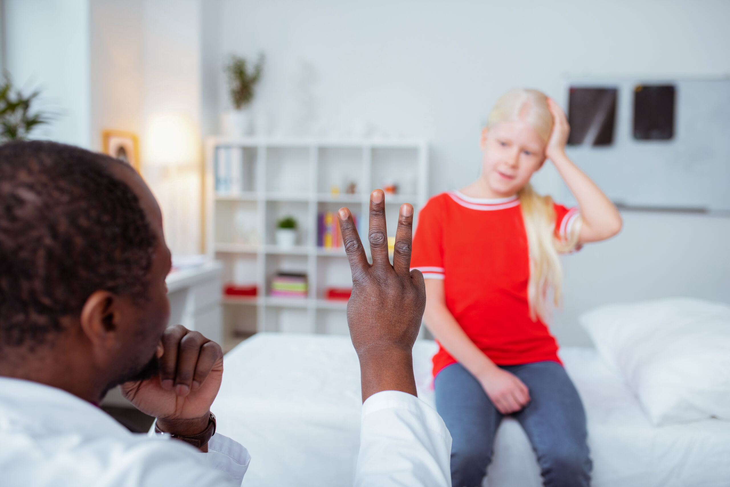 Dark skinned doctor showing girl with concussion three fingers